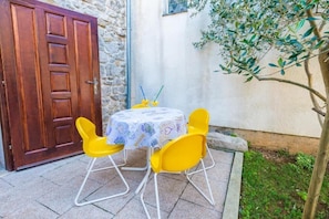 Eine Terrasse mit einem runden Tisch und vier gelben Stühlen, einer Holztür und einem Baum.