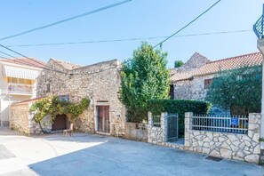 Une rue étroite bordée d’immeubles en pierre, avec une grille en métal et un banc.