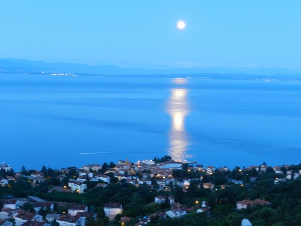 Un pueblo costero al atardecer, con un mar tranquilo que refleja la luz de la luna.