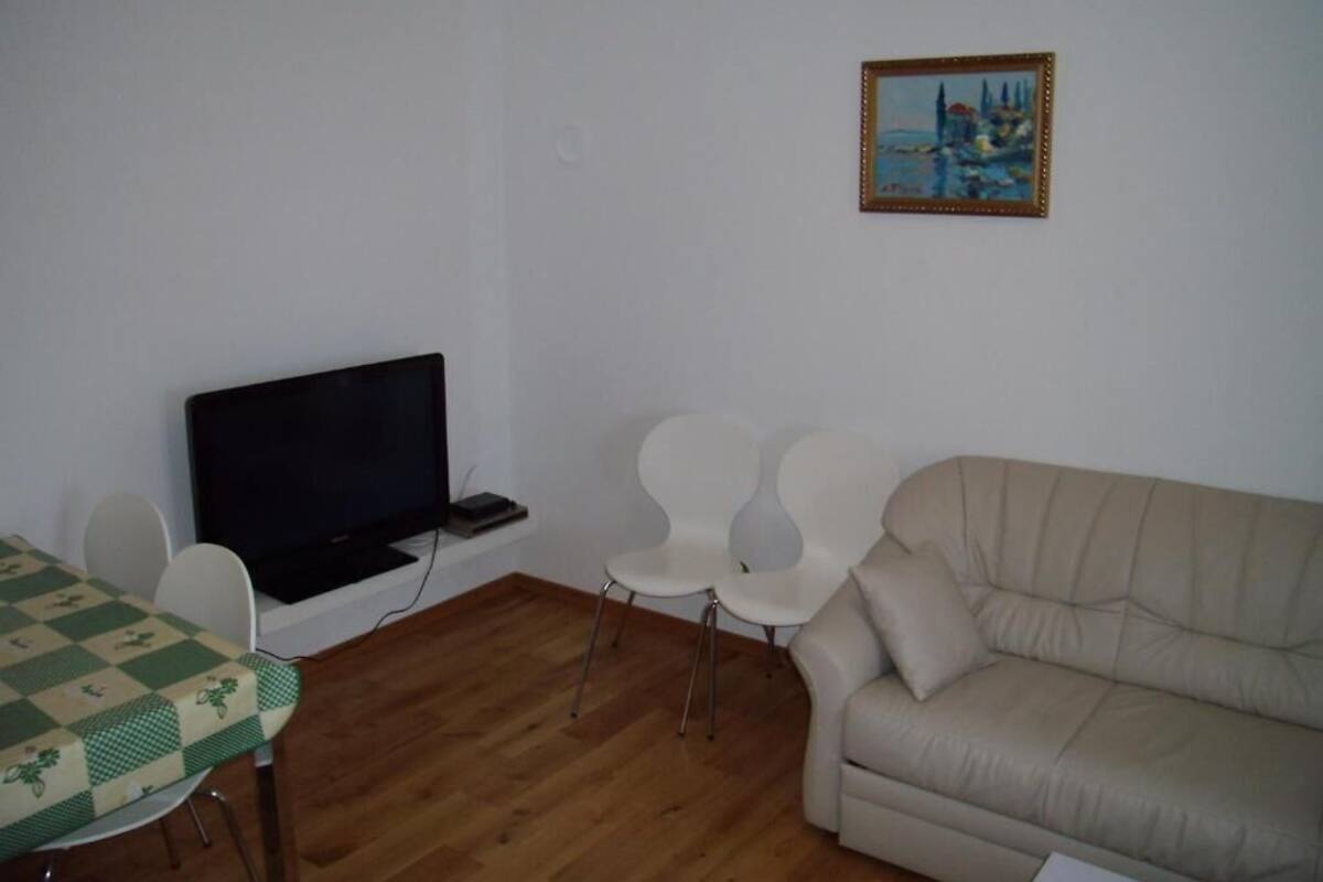 A living room with a television, two white chairs, a beige sofa, and a painting on the wall.