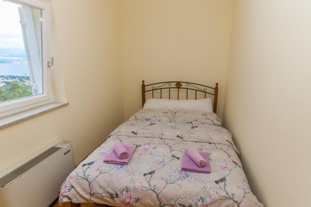 A small, single-bed room with a metal headboard, floral bedding, and two rolled towels on the bed.