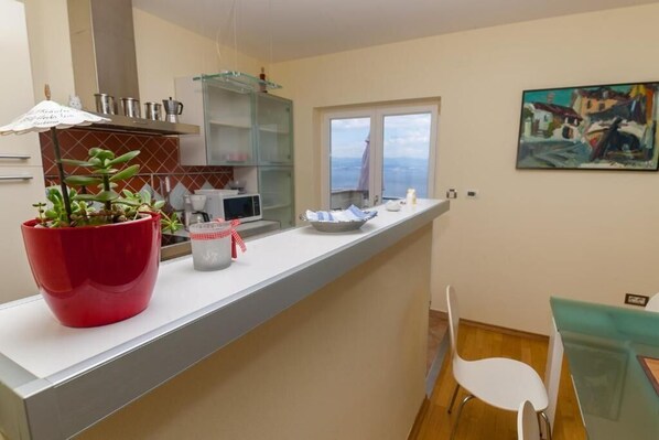 Cozinha moderna com bancada branca, uma planta vermelha e janela com vista.