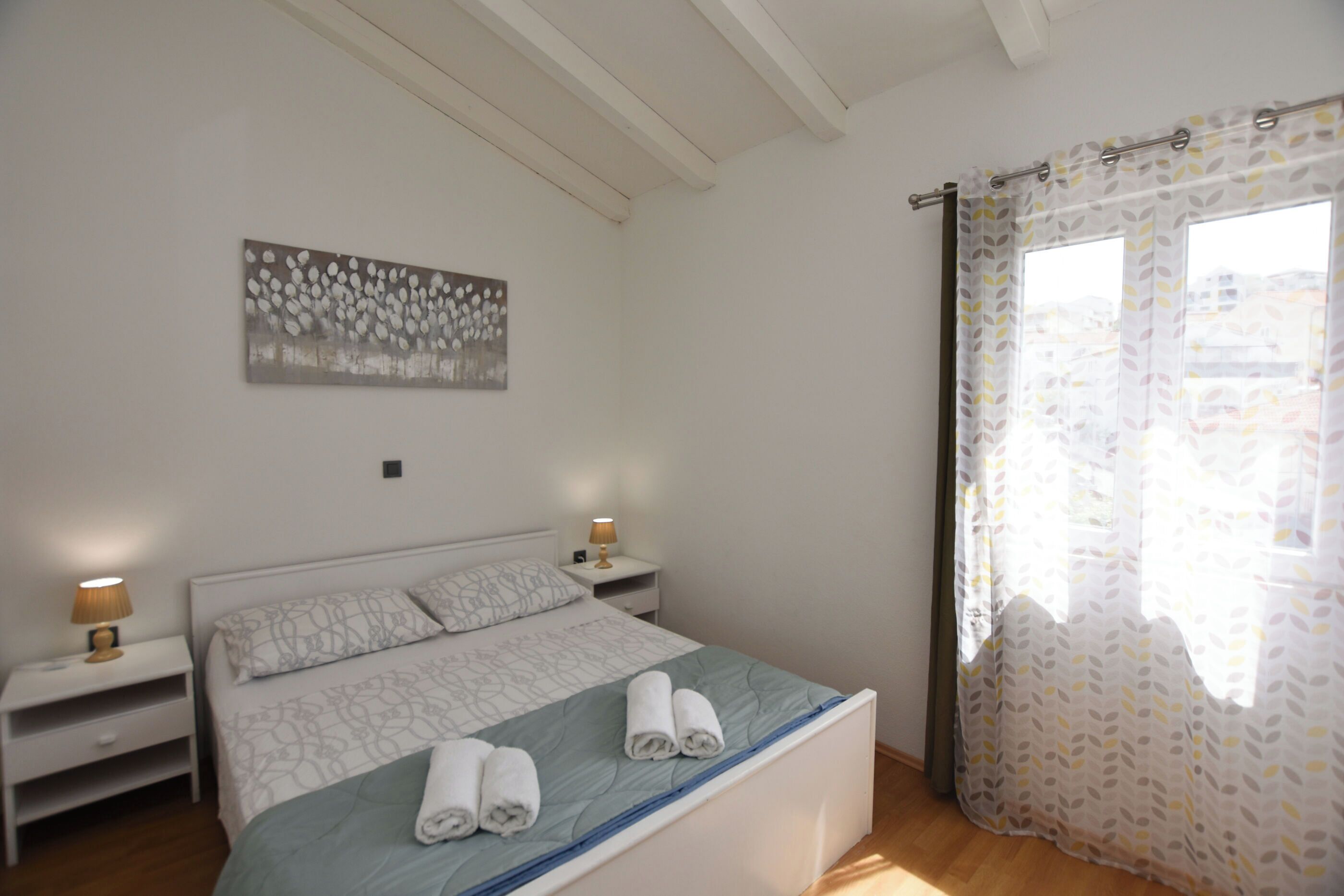 A bedroom with a bed, nightstands, a wall art piece, and a window with curtains.