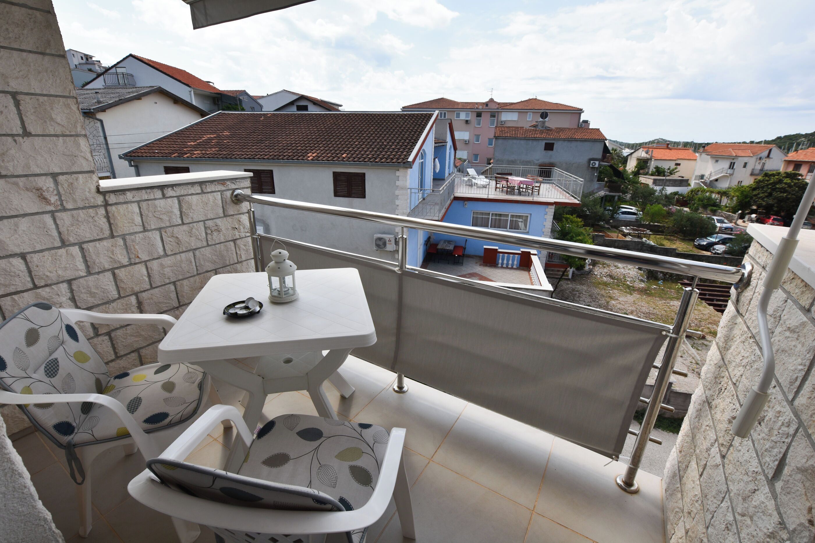 A balcony with a table and chairs, a view of neighboring buildings, and a railing.