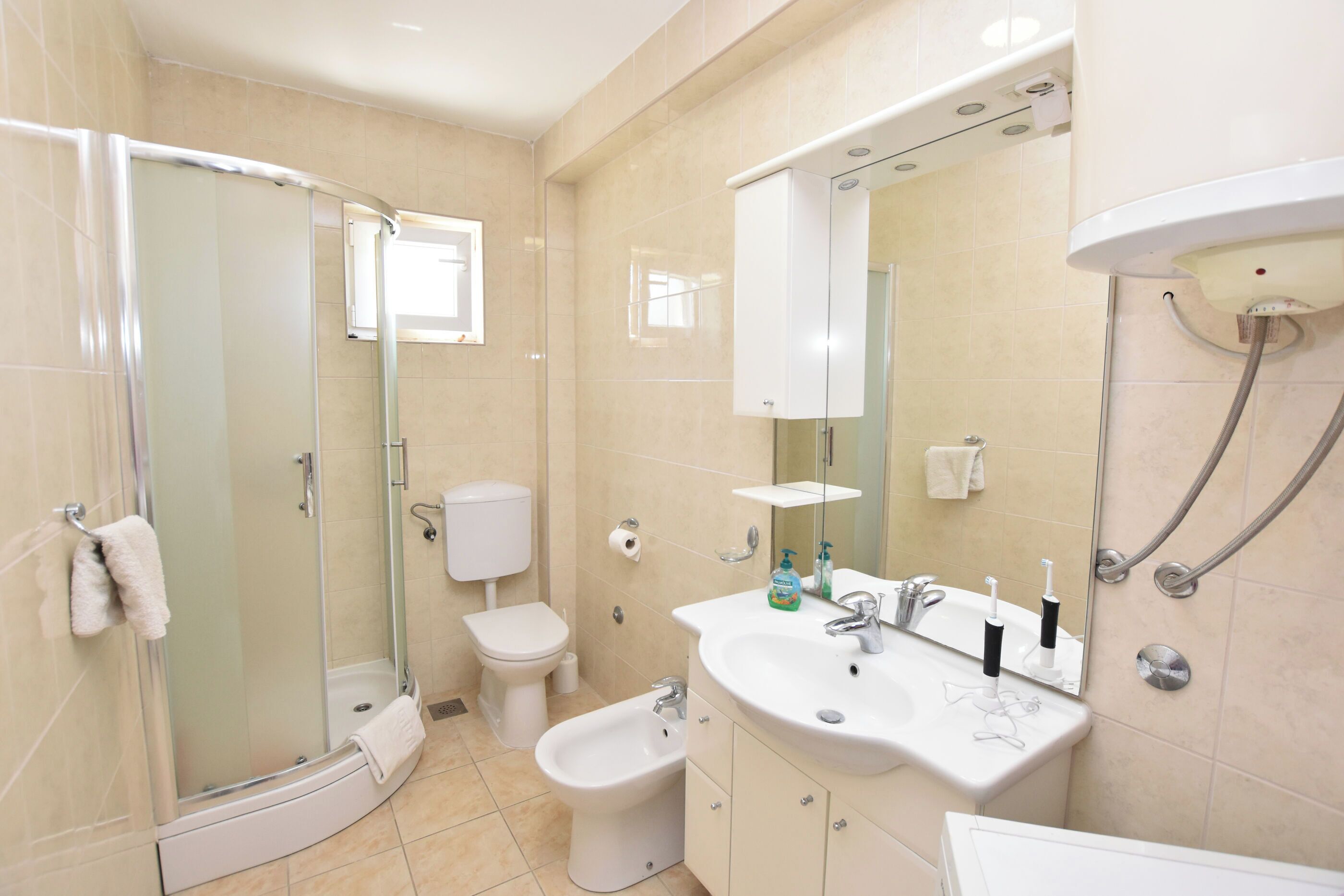 Une salle de bain moderne dotée d’une douche à parois de verre, de toilettes, d’un bidet et d’un lavabo avec un miroir au-dessus.