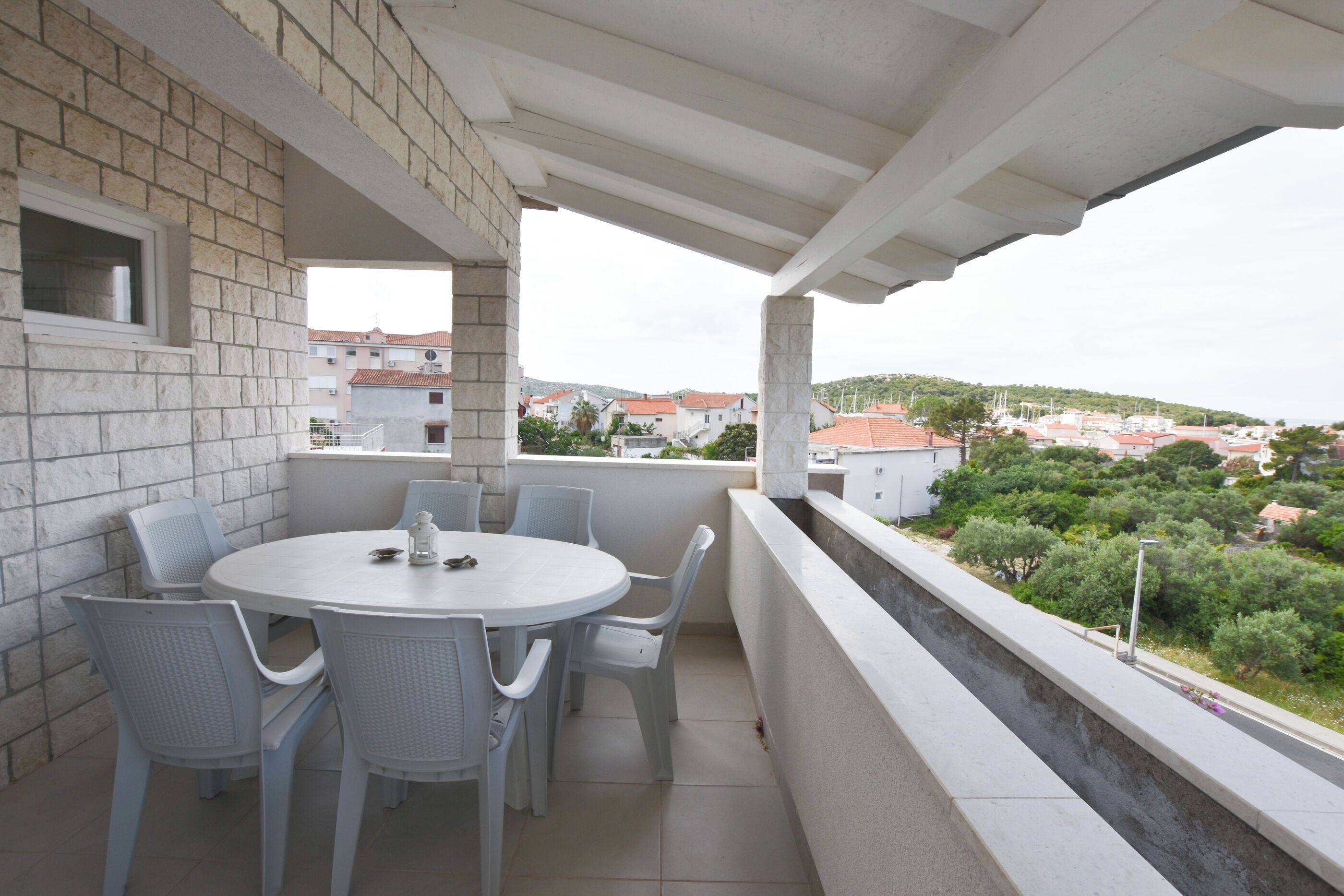 Ein Balkon mit rundem Tisch und Stühlen, Blick auf die Stadt und eine Steinmauer.