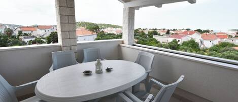 A balcony with a round table and chairs, overlooking a residential area with red-roofed houses.
