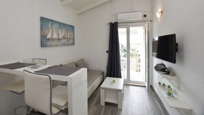 Ένας μοντέρνος, καλά φωτισμένος χώρος με τραπεζαρία, έναν καναπέ, μια τηλεόραση και ένα μπαλκόνι με θέα.