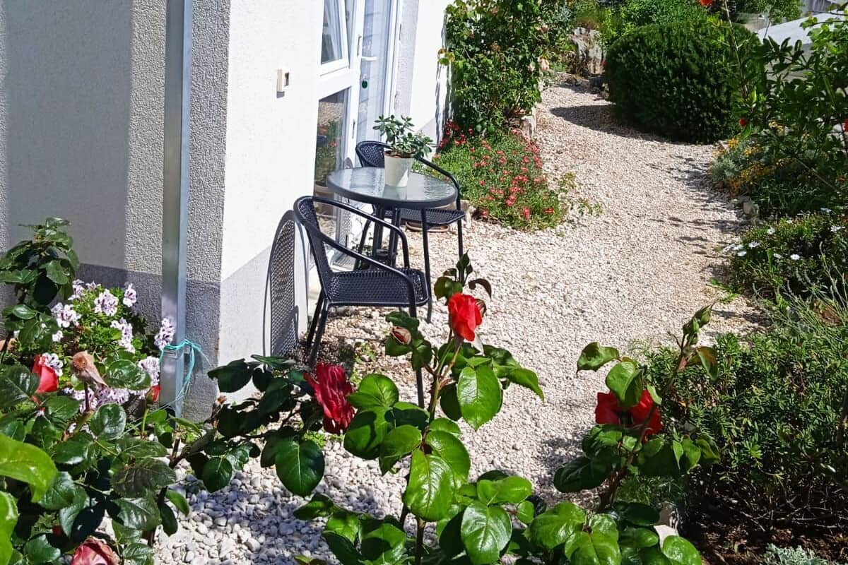 A white building with a gravel pathway leading to a table and chairs outside.