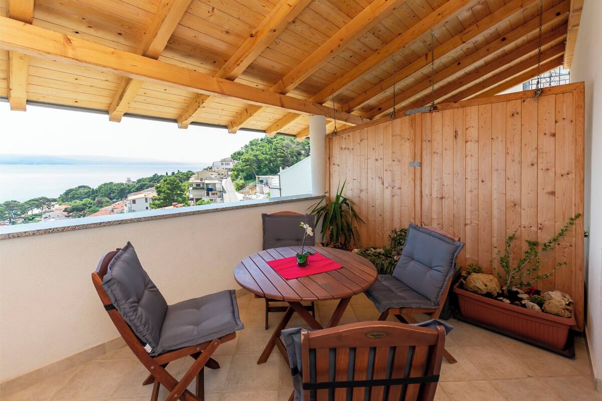 A wooden deck with a round table and four chairs, overlooking a scenic view of a coastal town.