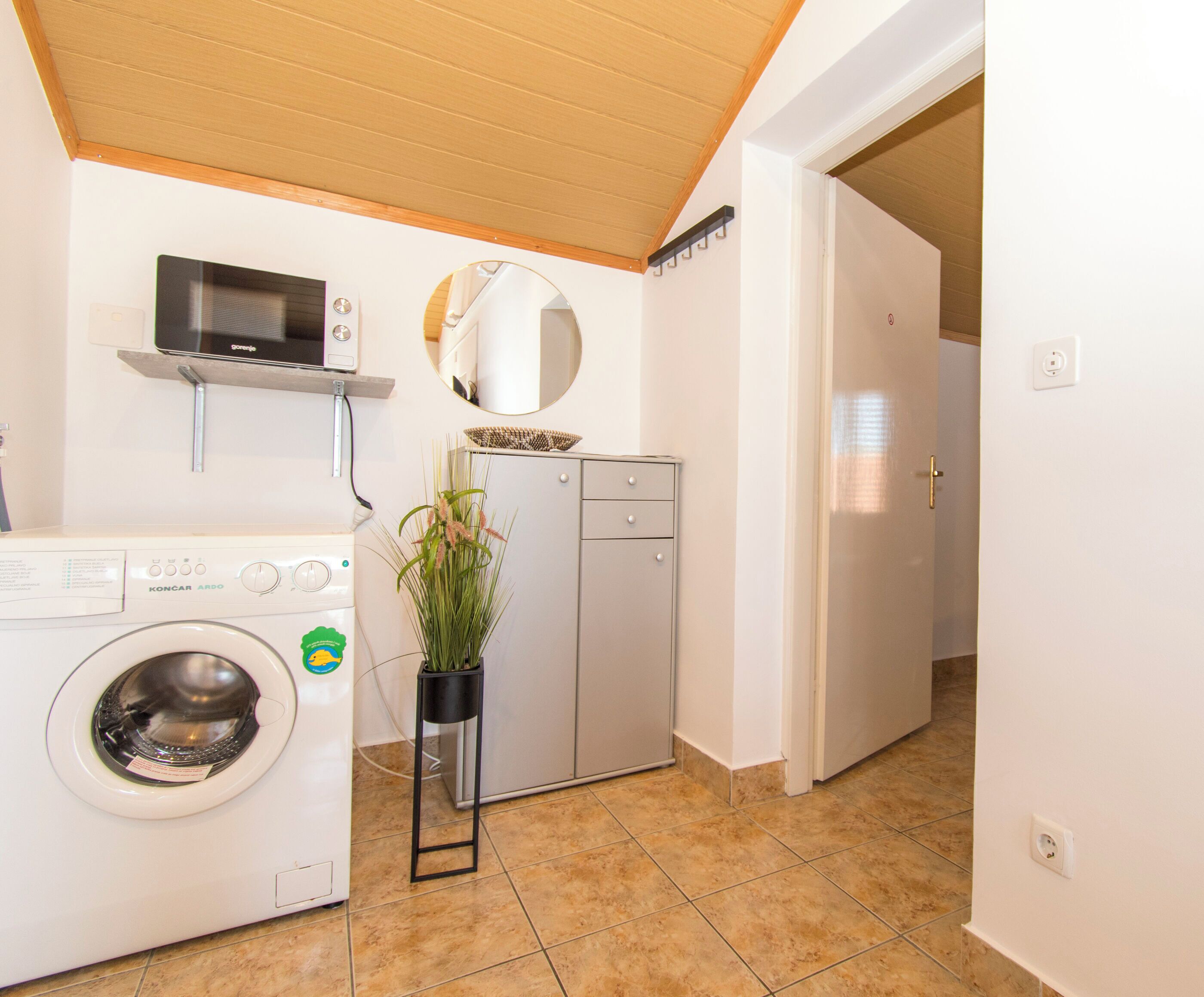 A compact laundry room with a washing machine, a dryer, a microwave, and a potted plant.