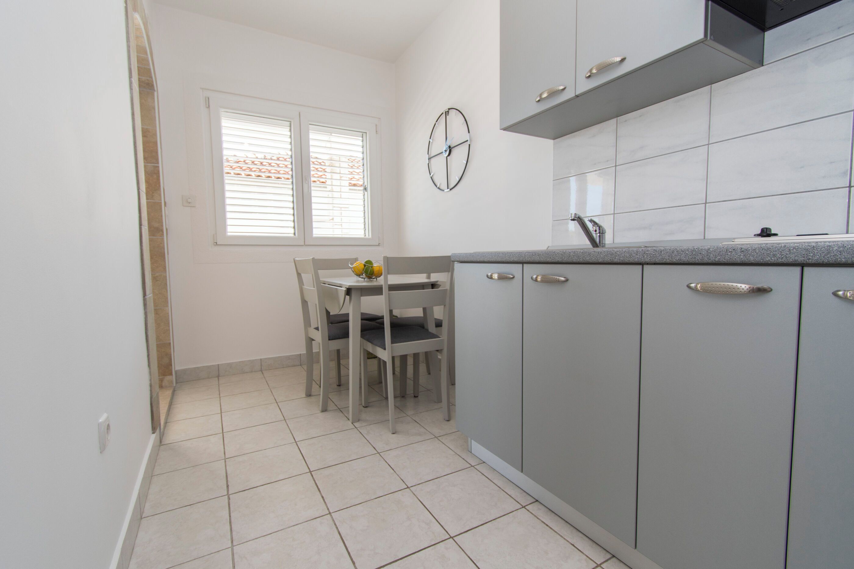 A kitchen with grey cabinets, a white countertop, and a dining area with a table and chairs.