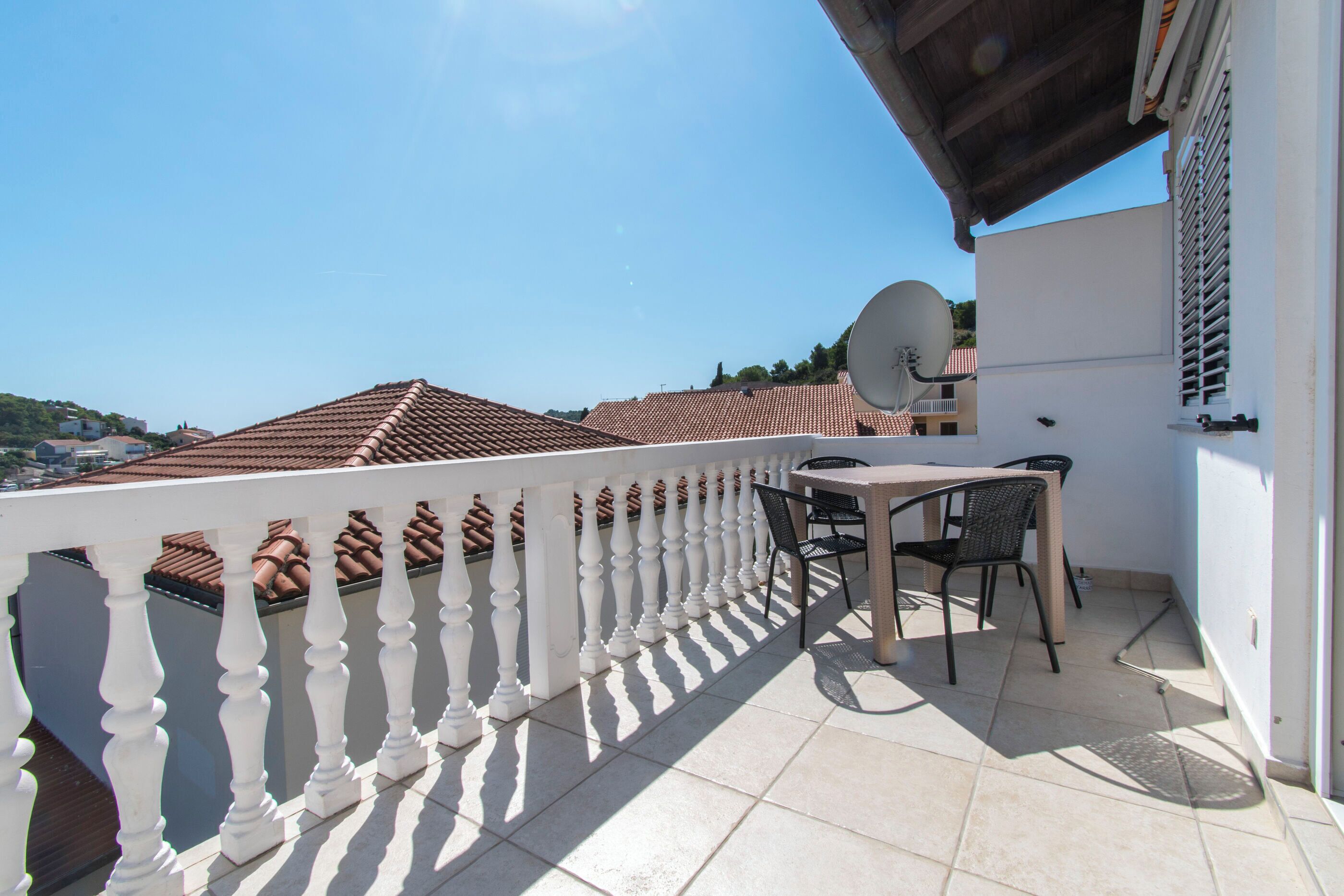 A balcony with a white balustrade, a table with chairs, and a satellite dish.