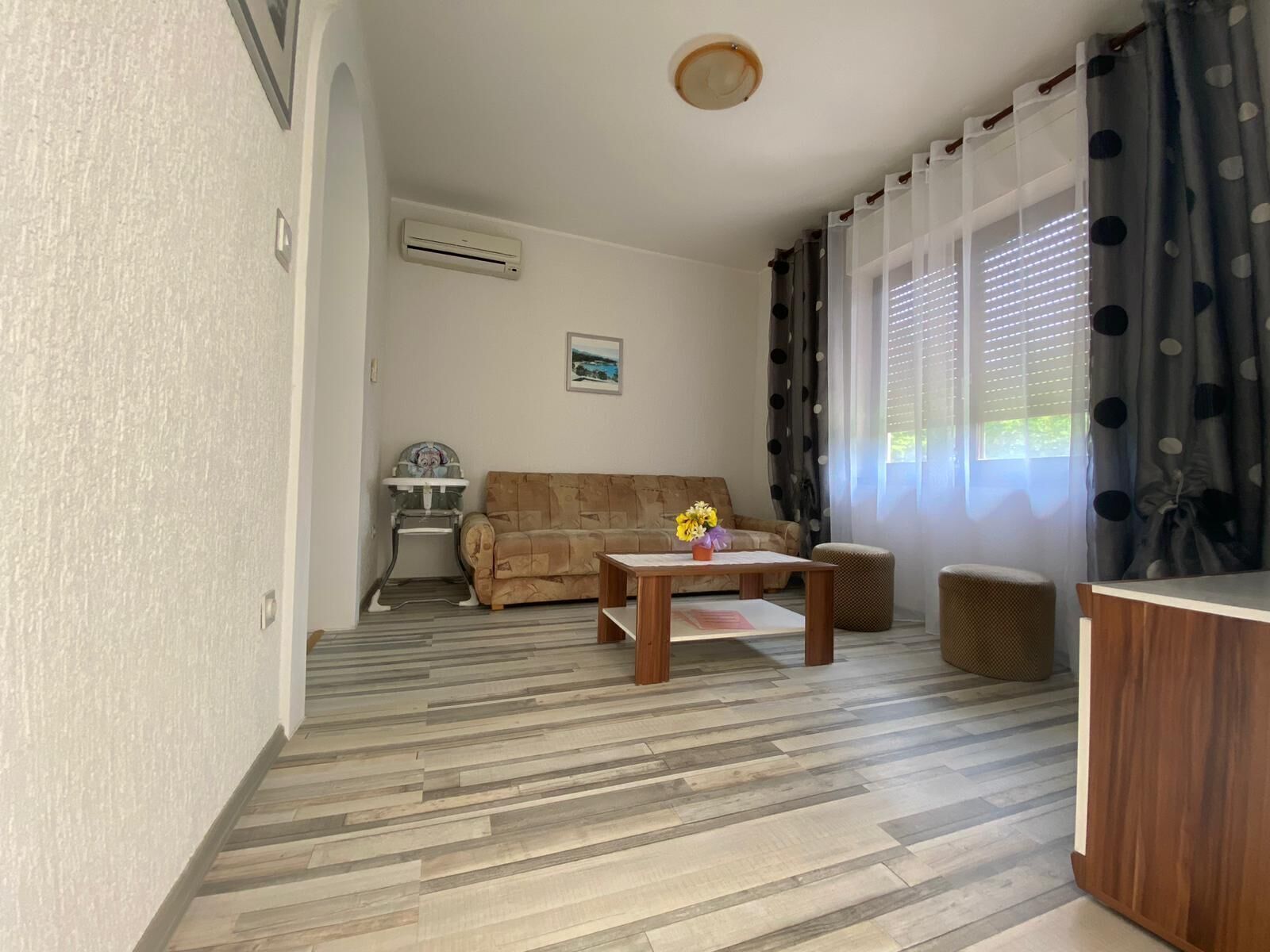 Una sala de estar con un sofá, una mesa de centro, un balancín para bebé y una ventana con cortinas.