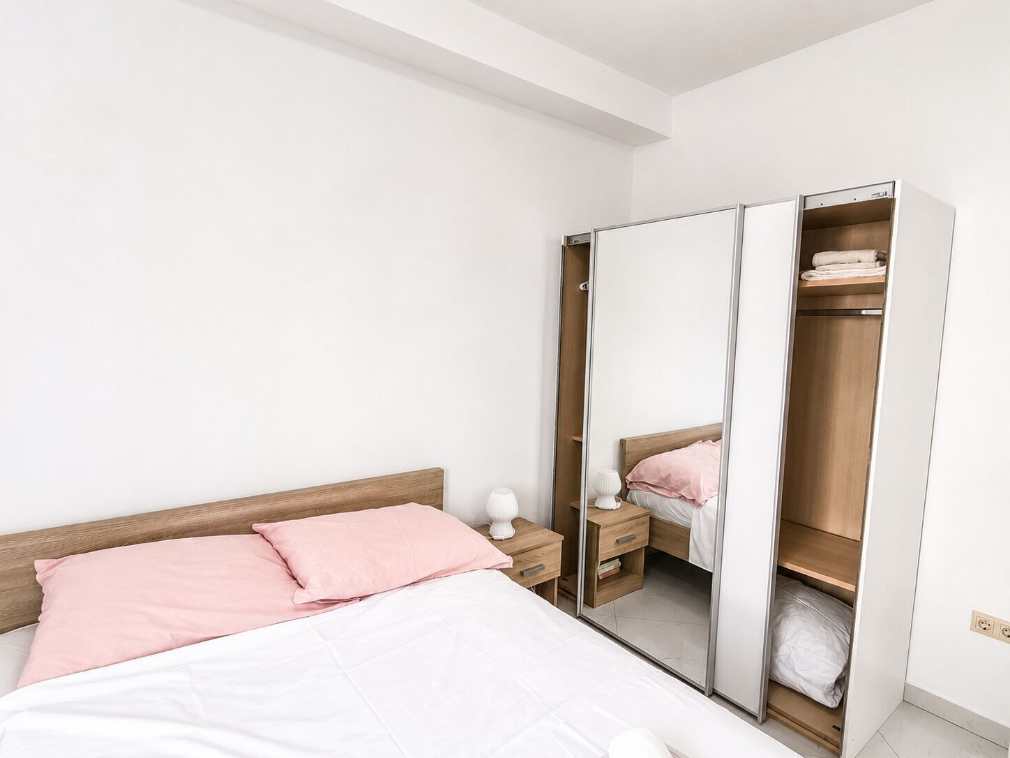 A bedroom with a bed, a nightstand, a wardrobe, and a mirror.