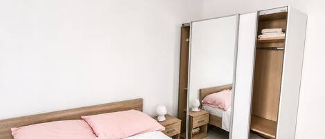 A bedroom with a bed, a nightstand, a wardrobe, and a mirror.