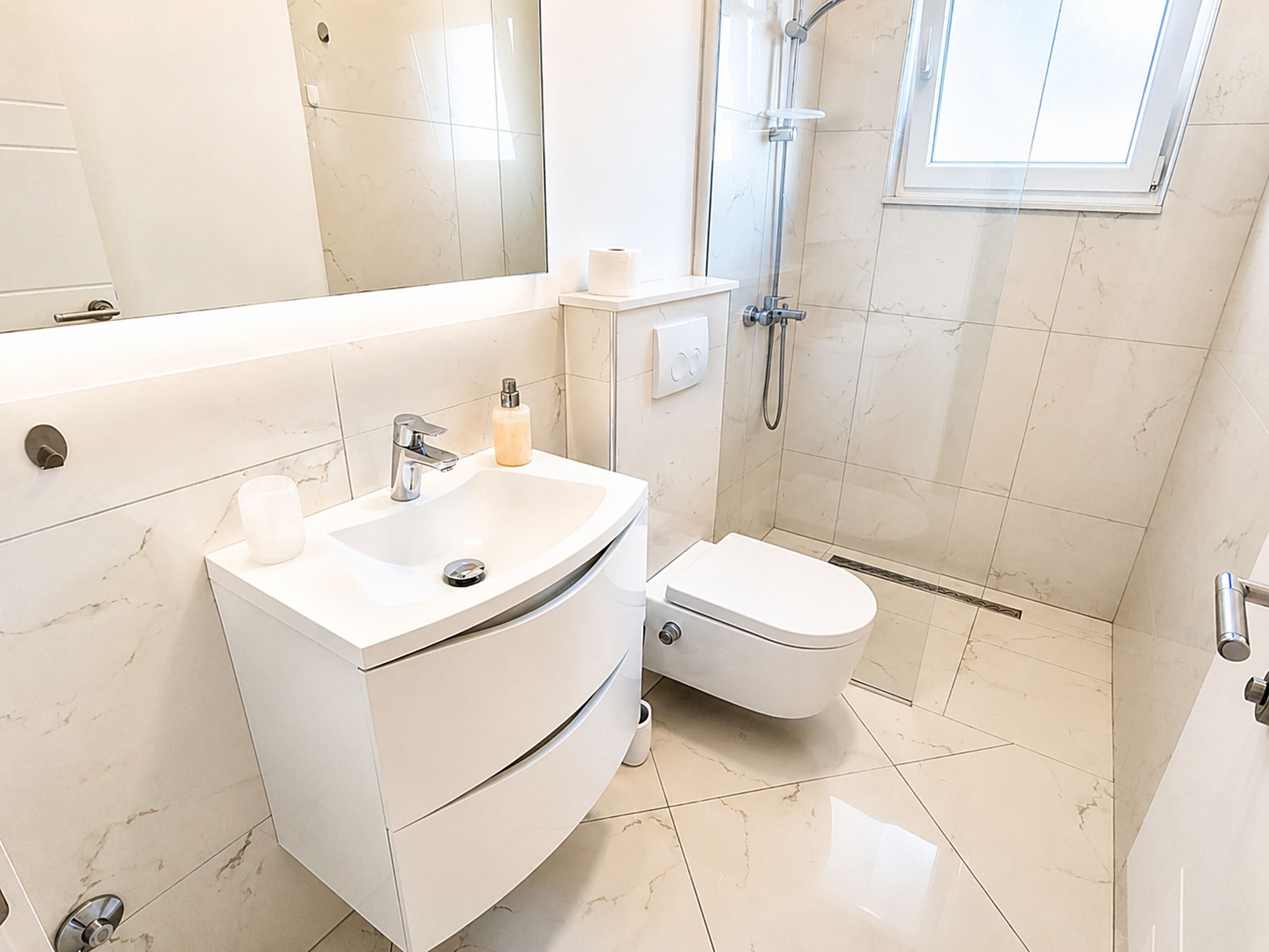 A modern bathroom with a white vanity, sink, and toilet.
