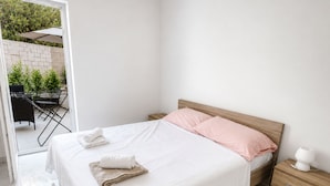 Une chambre à coucher comprenant un lit, une table de chevet, une commode et donnant sur un patio extérieur.