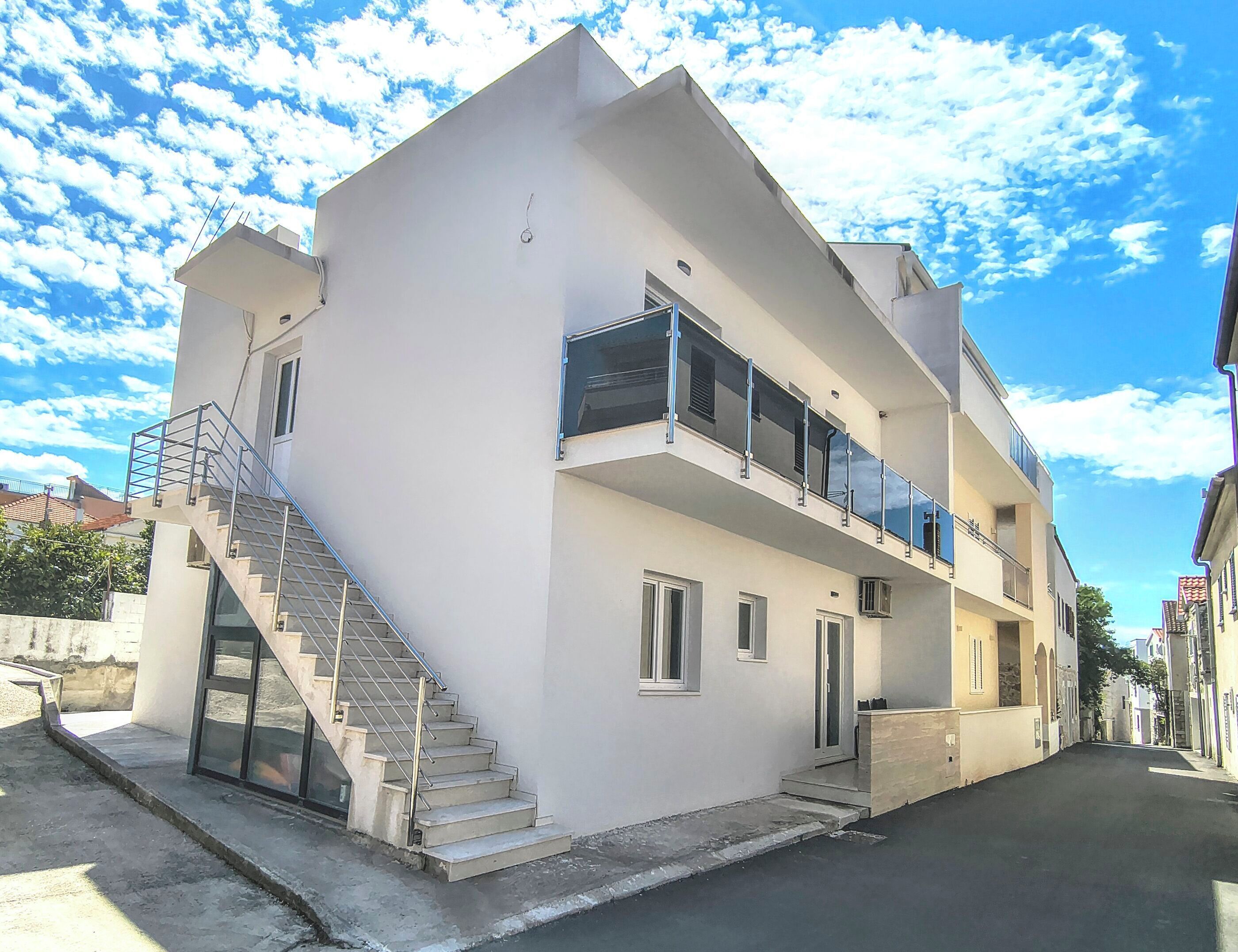 A modern two-story building with a staircase, balconies, and a clear sky.