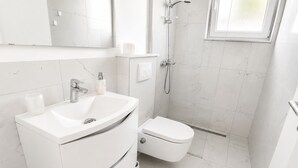 Une salle de bain moderne avec un meuble-lavabo blanc, des toilettes et une douche.