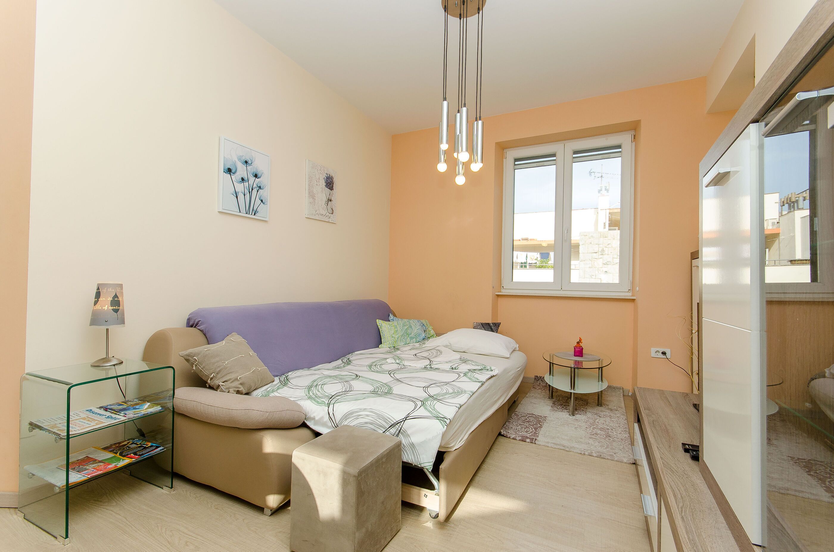 A modern bedroom with a bed, a glass side table, a small round table, and a window with a view.