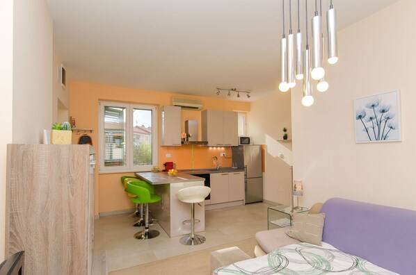 A compact kitchen with a dining area, a sofa, and a small table with a lamp. - Apartment City Light (Split)