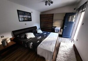 Ein Schlafzimmer mit Bett, Nachttisch, Kommode, einem Fenster mit Vorhängen und einer Tür.
