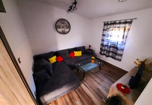 Una sala de estar con un sofá, una mesa de centro de vidrio, un reloj y una ventana con cortinas.