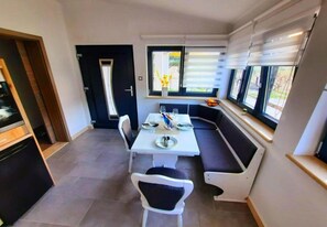 Ein Essbereich mit einem weißen Tisch, einer schwarzen gepolsterten Bank und einem Fenster mit Jalousien.