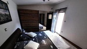 Ein Schlafzimmer mit Bett, einer Wand mit Holzvertäfelung, einem Fenster mit Vorhängen und Blick ins Freie.