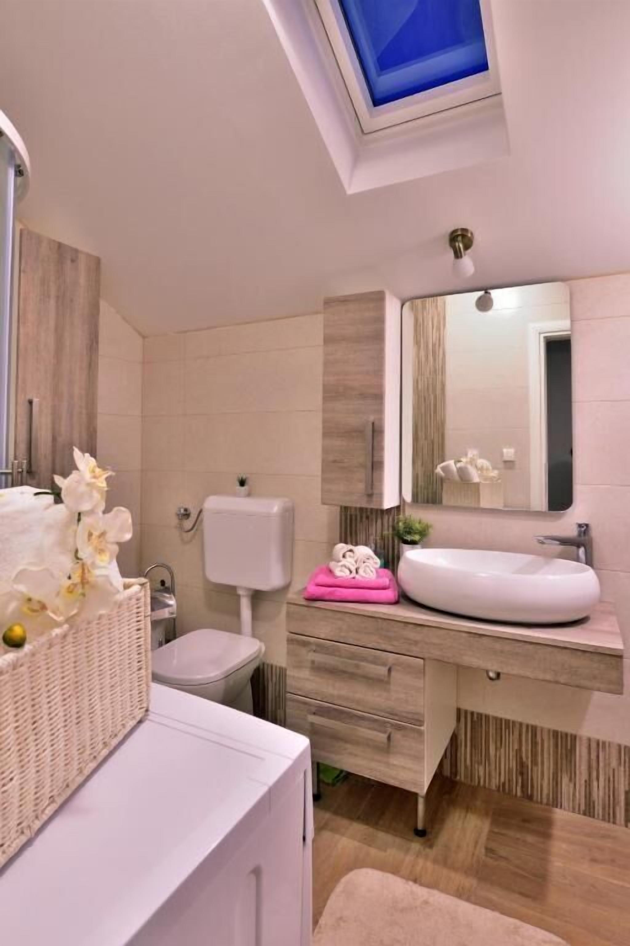 A modern bathroom with a skylight, a white sink, a toilet, and a wicker basket with flowers.
