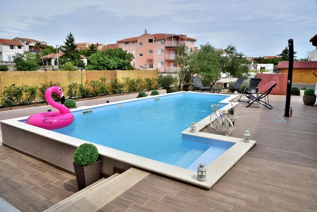 A rectangular swimming pool with a pink flamingo float, surrounded by a wooden deck and a low brick wall.