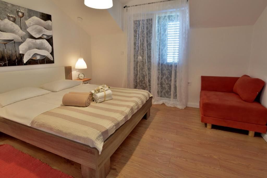 Une chambre à coucher avec un lit en bois, un canapé rouge, un tableau au mur et une fenêtre ornée de rideaux légers.