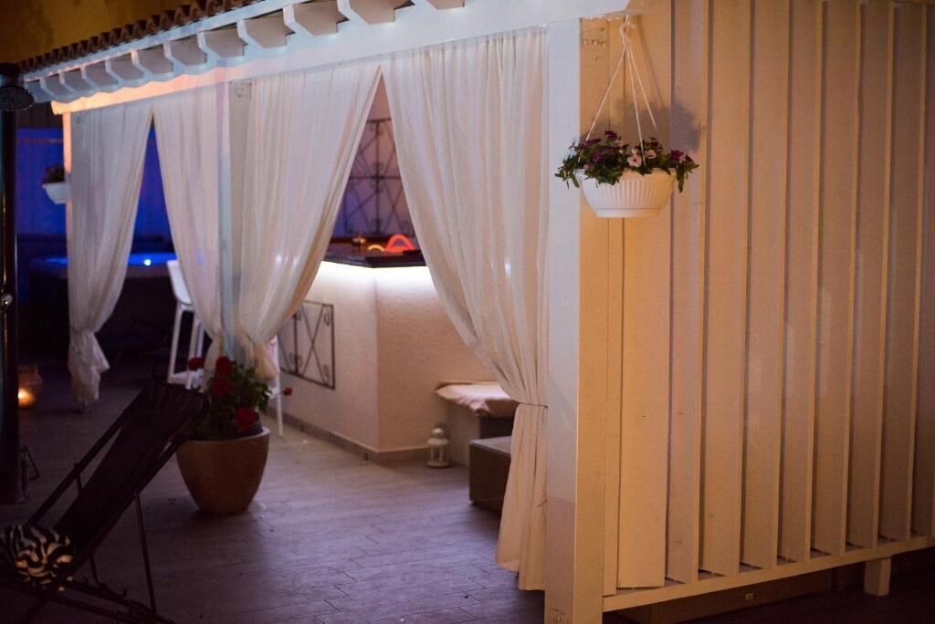 A covered outdoor seating area with white curtains, a hanging flower pot, and a wooden fence.