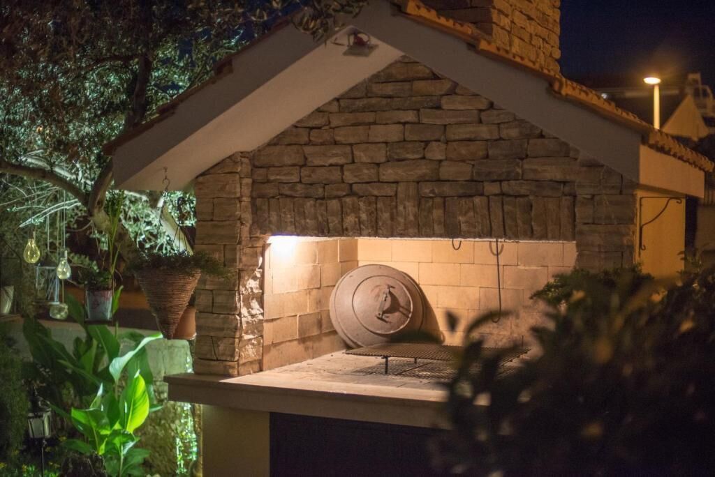 A stone-built outdoor kitchen with a built-in grill, surrounded by potted plants.