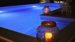 Une piscine dont le bord est illuminé de lumière bleue, avec deux bougies allumées posées sur une étagère.