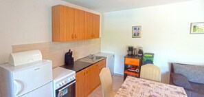 A compact kitchen with a refrigerator, stove, sink, and wooden cabinets. There is a dining table with a chair and a couch in the adjacent living area. - House Stone Curlew 5 (Benkovac)