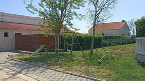 Egy lakóingatlan, amelyhez tartozik egy kiépített felhajtó, egy fa garázskapu, egy hintaállvány és egy kőből épült épület, vörös cseréptetővel.