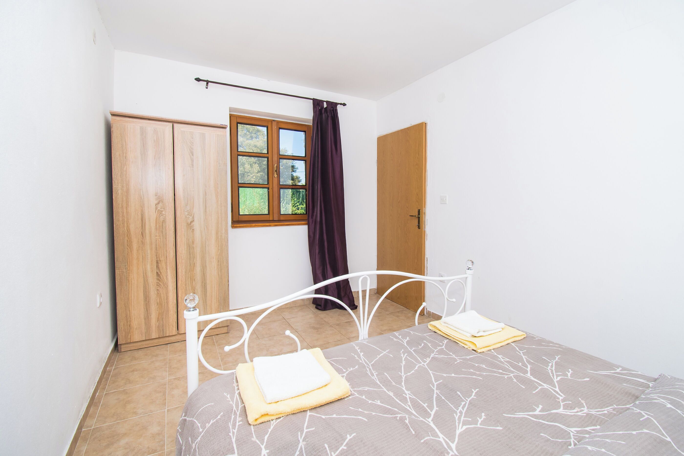 A bedroom with a bed, a wardrobe, a window with curtains, and a door.