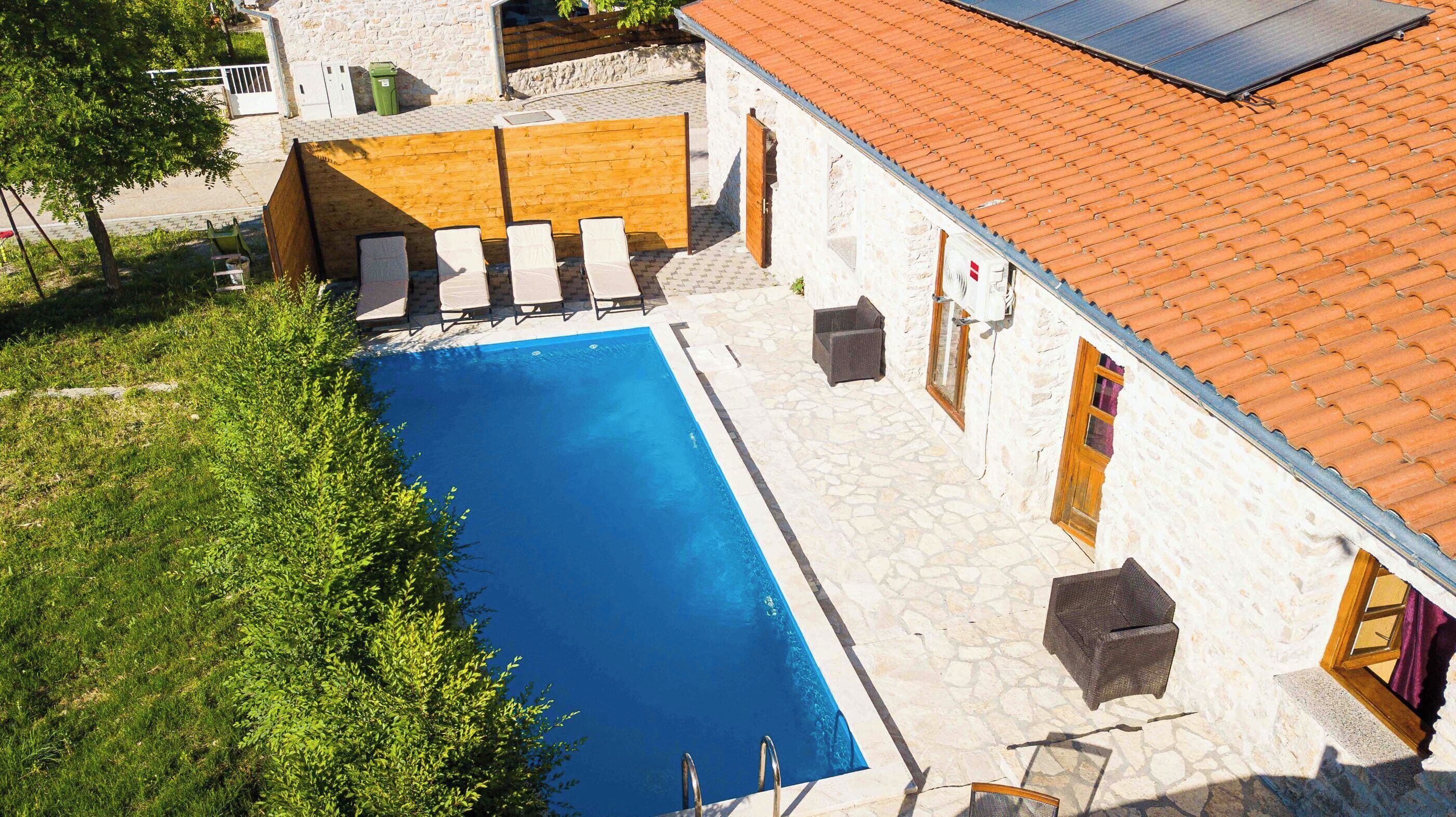 A swimming pool with lounge chairs, a stone building with a tiled roof, and a solar panel.