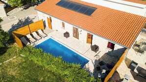Egy medencével, kőfalakkal és cserépfedeles tetővel rendelkező villa.