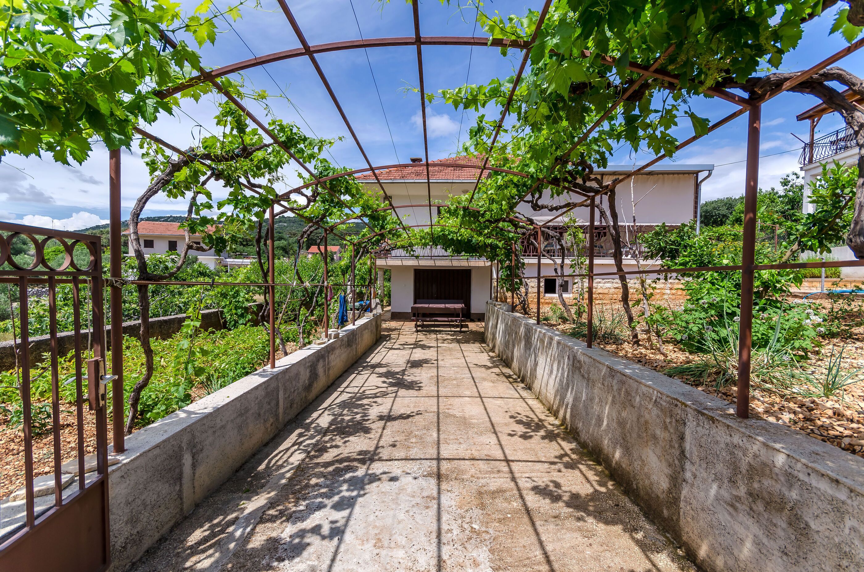 A pathway leading to a building with a red roof, surrounded by greenery and a metal fence.