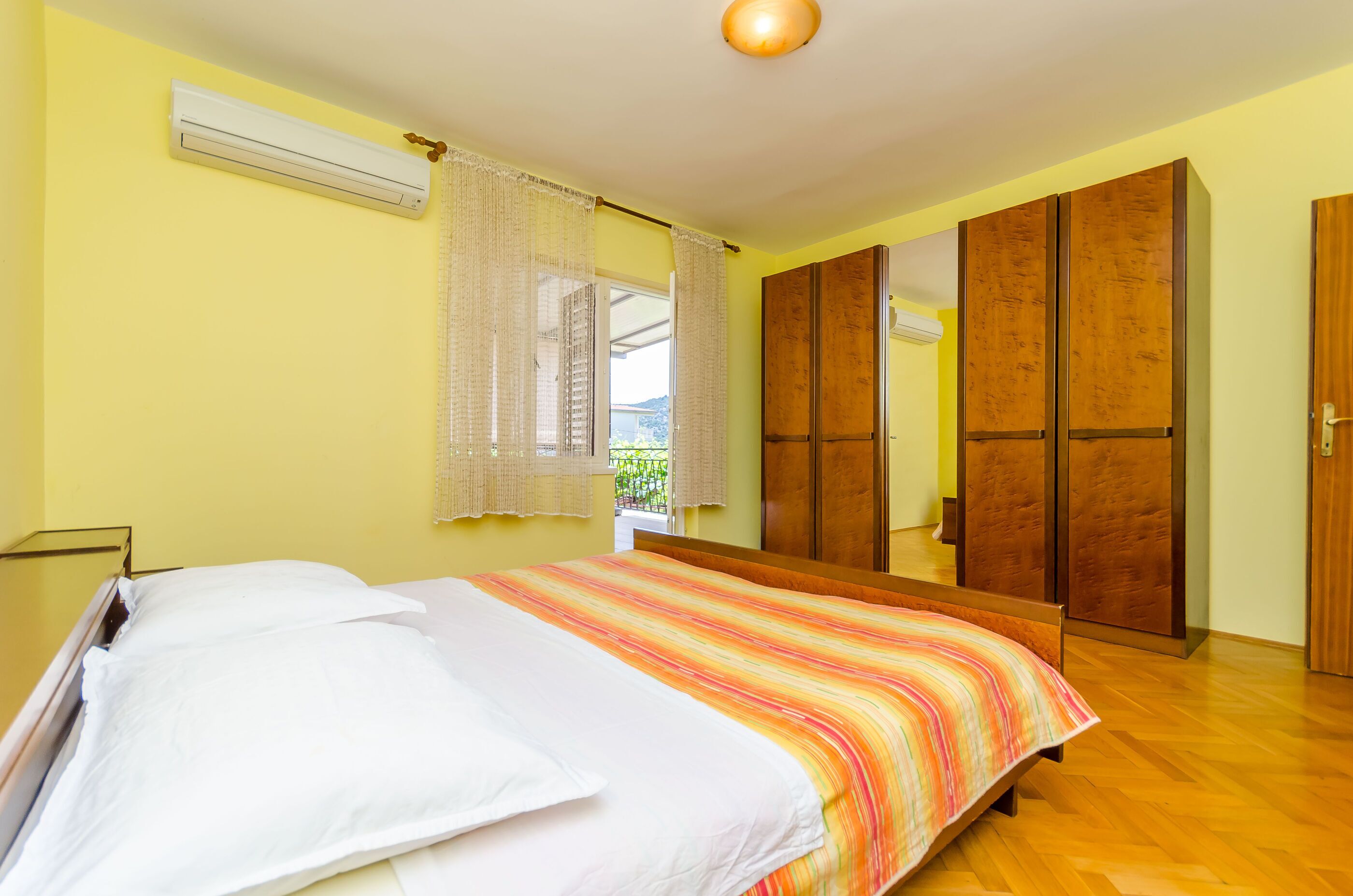 A bedroom with a bed, a wardrobe, and an air conditioning unit.