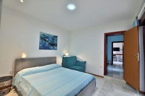 A bedroom with a bed, bedside lamps, a painting, and a door leading to a bathroom. - Apartments Caterina (Pula)