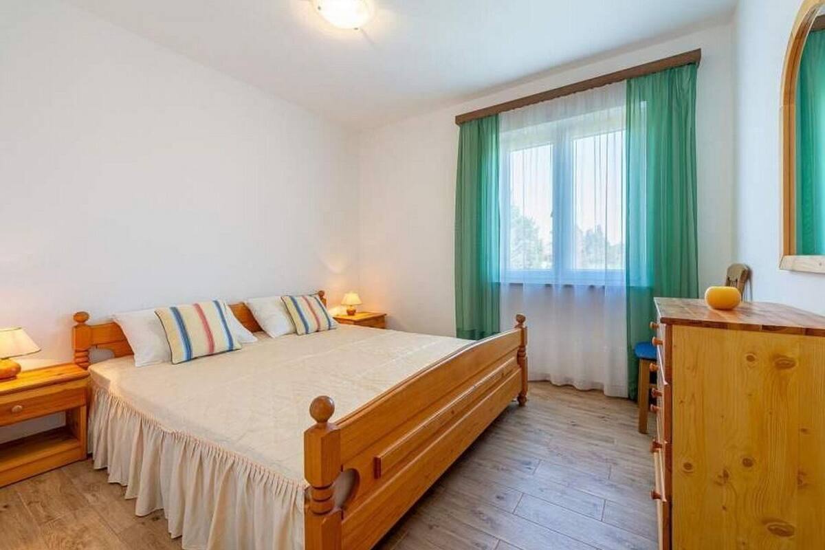 A bedroom with a wooden bed, a nightstand, a dresser, and a window with curtains.