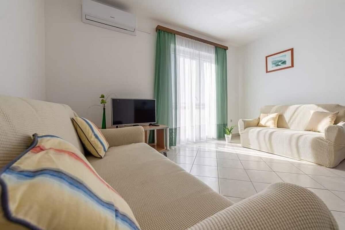 A living room with two sofas, a TV, and a window with green curtains.