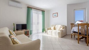 Ein Wohnzimmer mit Sofa, Fernseher, Esstisch mit Stühlen und einem Fenster mit Aussicht.