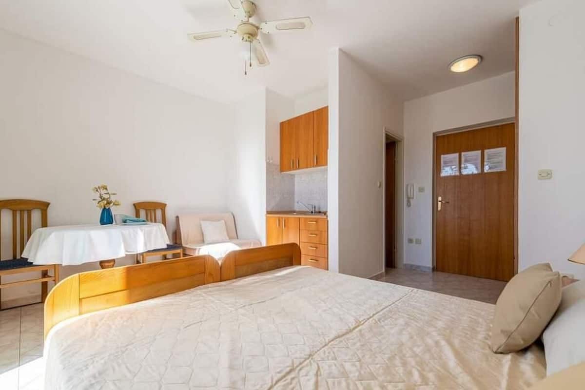 A bedroom with a large bed, wooden headboard, a small table with chairs, a ceiling fan, and a wooden wardrobe.