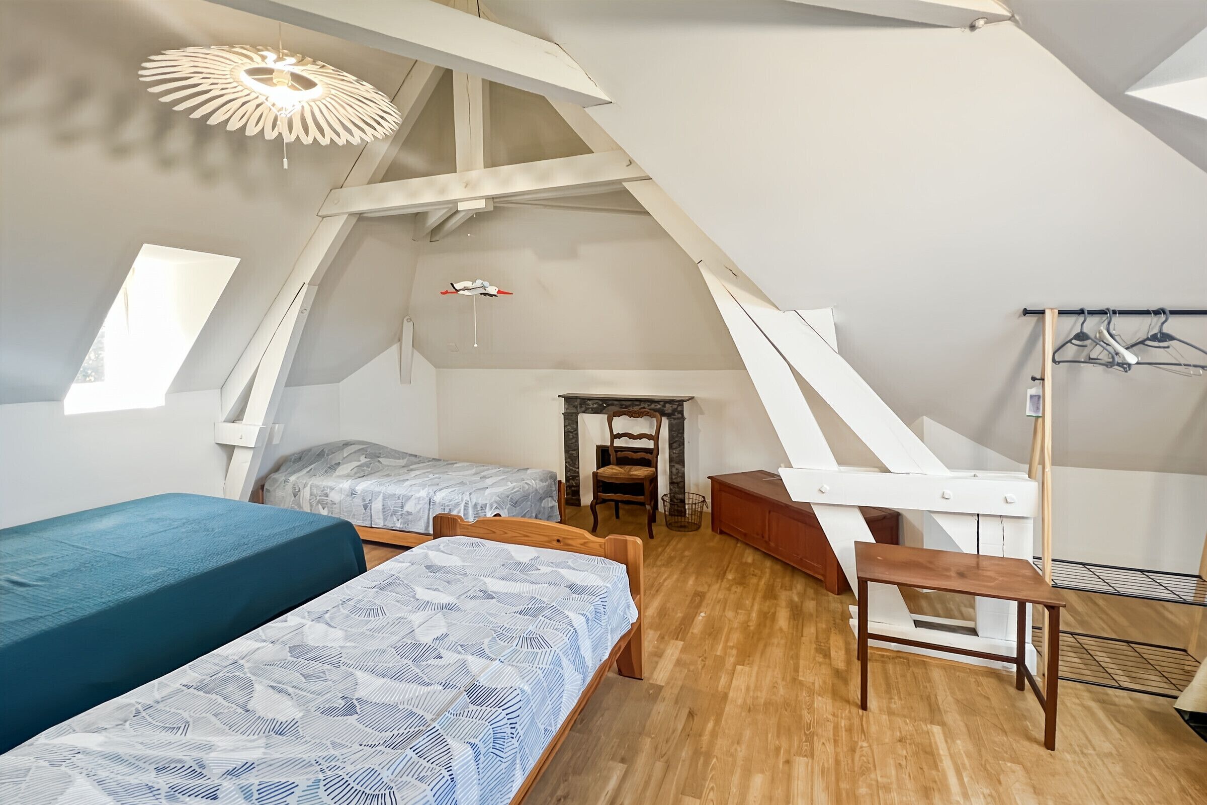 Ett sovrum i loftstil med två sängar, en träbänk, en hängande lampa och en garderob med en spegel.