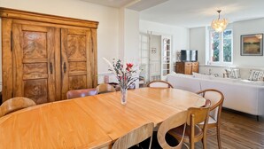 A dining area with a wooden table and chairs, a vase with flowers, and a white sofa in the background. - Renovated family home 14 sleeps 10 min from beaches, parking and wifi (Quéven)